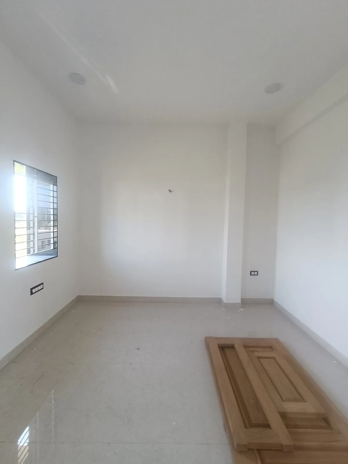 The bedroom before: an empty room with bare walls, a window on the left and removed door panels on the floor